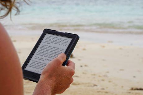 Person sitting on the beach reading from a tablet.