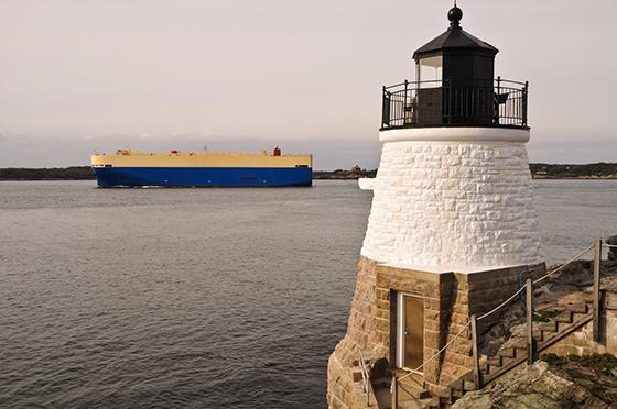 image of lighthouse in foreground with container ship on calm waters in background